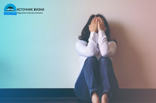 Женщина сидит на полу, закрыв лицо руками
